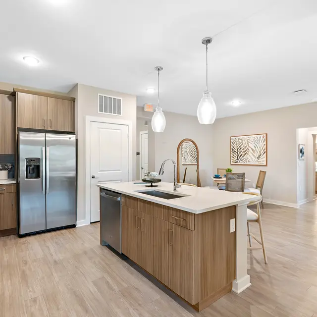 Contemporary Kitchen Design A modern kitchen featuring wooden cabinets, stainless steel appliances, and an island with bar stools. The space is bright and open, with a living area visible in the background.