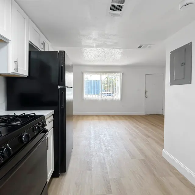 Modern Kitchen Apartment Interior An interior view of a modern kitchen with a gas stove and black refrigerator, featuring light-colored wooden flooring and white walls.