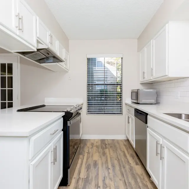 A modern kitchen with white cabinets, a black stove and a silver dishwasher, featuring a large countertop and natural light from a window.