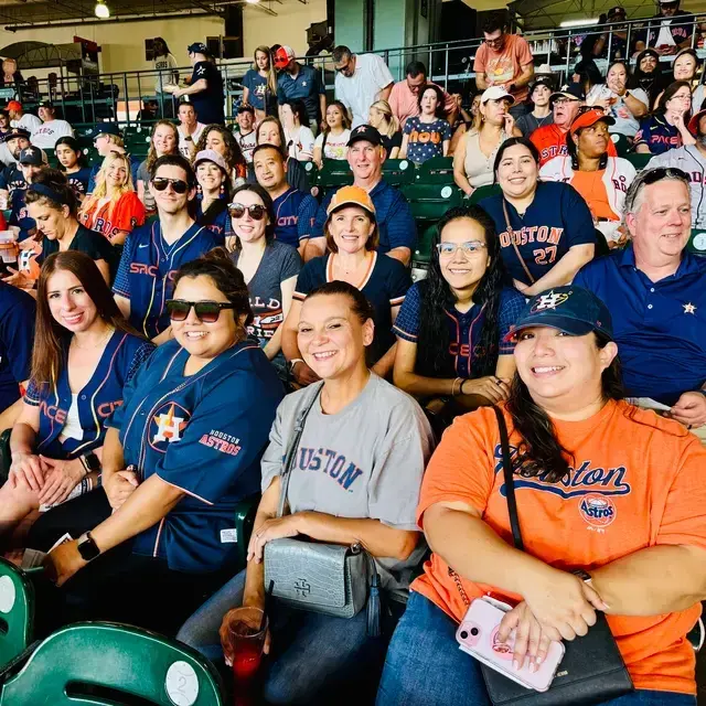 A group of baseball fans wearing team jerseys sitting in a stadium. They are smiling and enjoying the game, with some holding drinks.