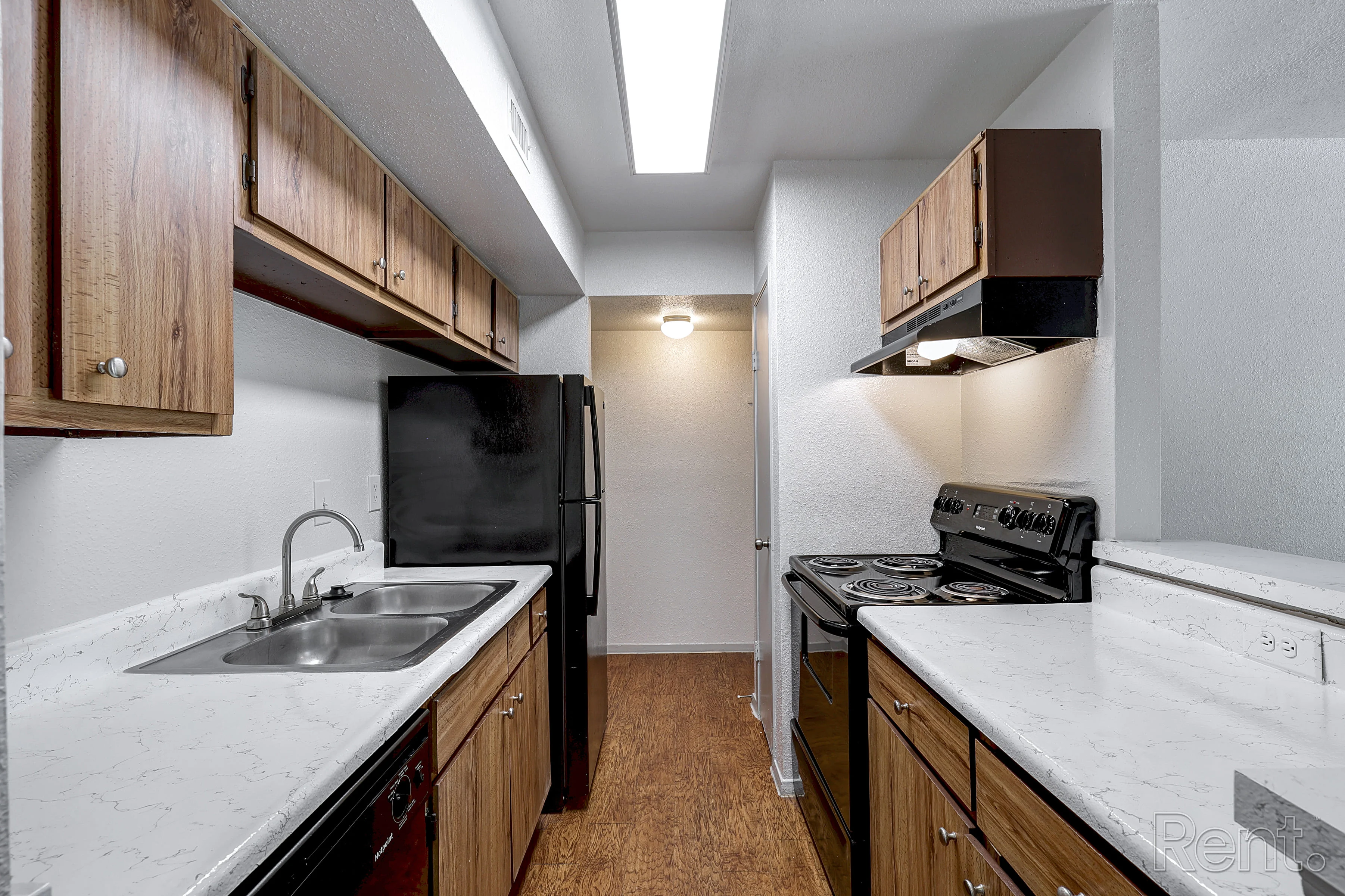 A modern kitchen featuring dark wood cabinetry, stainless steel appliances, and a double sink. The kitchen has a streamlined layout with a lighted ceiling and ample counter space.