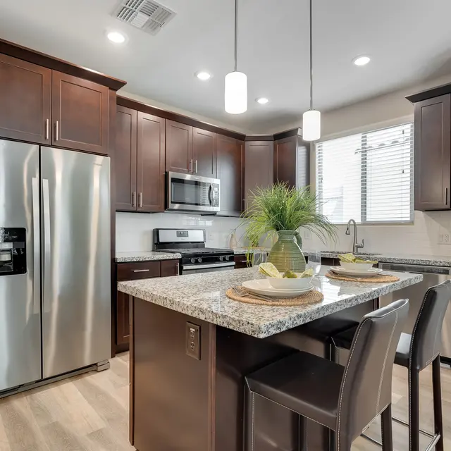 A modern kitchen featuring dark wooden cabinetry, stainless steel appliances, and a large island with granite countertops.