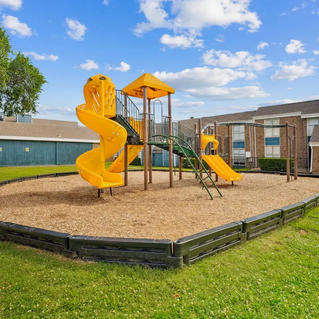 A vibrant playground featuring a yellow slide, climbing structures, and grassy surroundings under a partly cloudy sky.