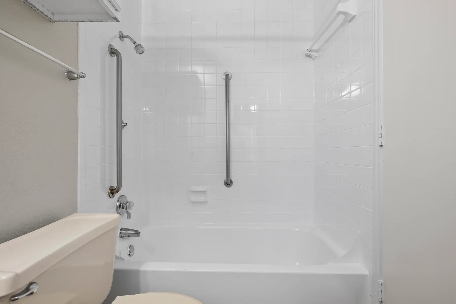 Clean bathroom with a white bathtub, toilet, and grab bars for safety.