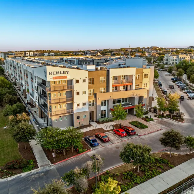 Aerial view of a modern apartment complex with a landscaped parking area and surrounding greenery.