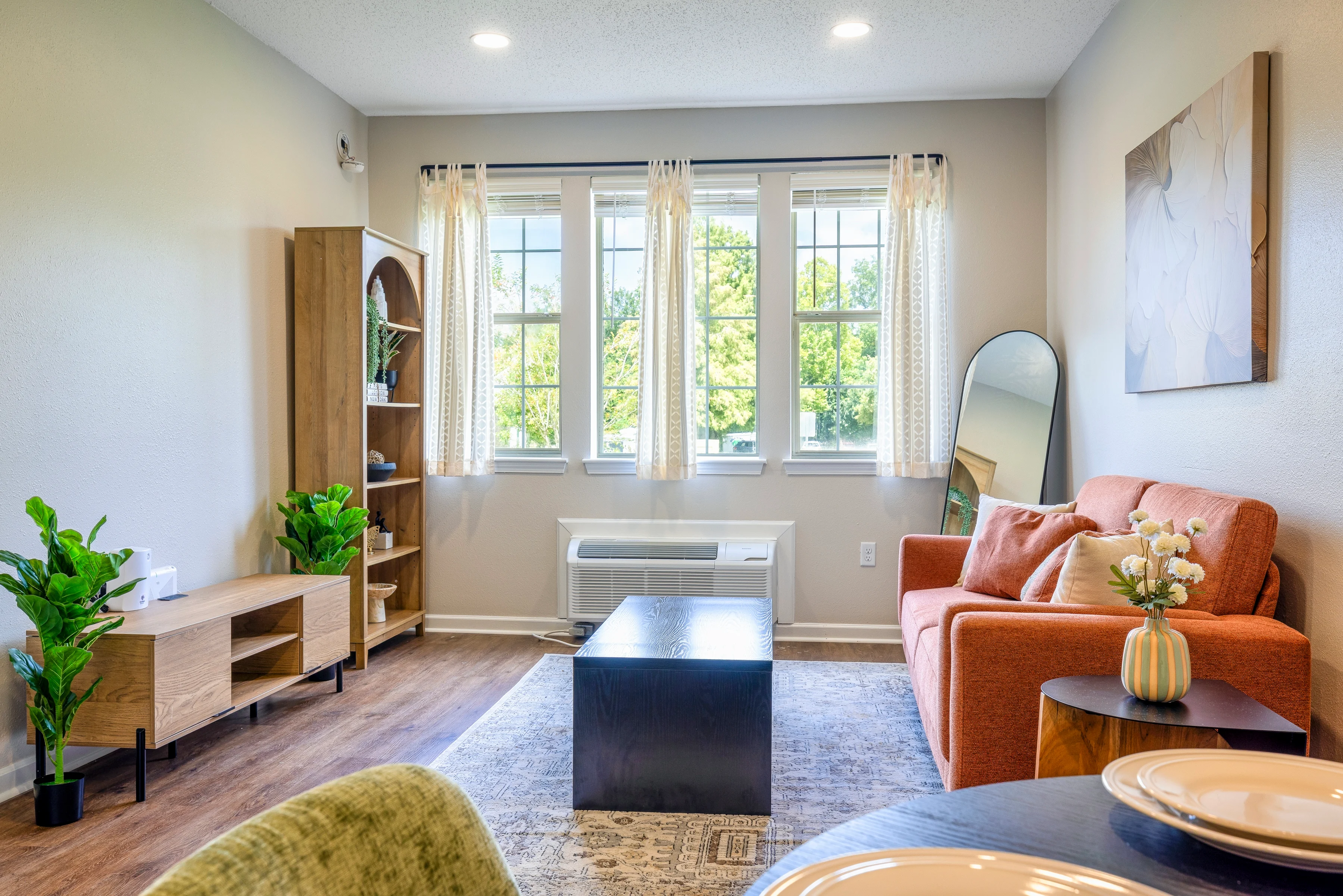 Modern Living Room Interior A bright and airy living room featuring a modern orange sofa, a coffee table, and a wooden TV stand with plants. Large windows allow natural light to fill the space.