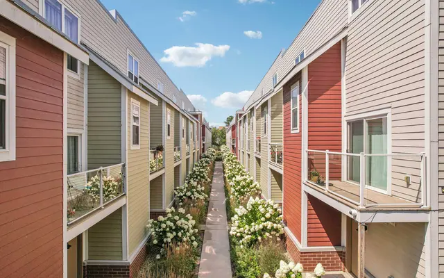 A view of a colorful apartment complex with two rows of buildings facing each other, separated by a flower-lined walkway under a blue sky.