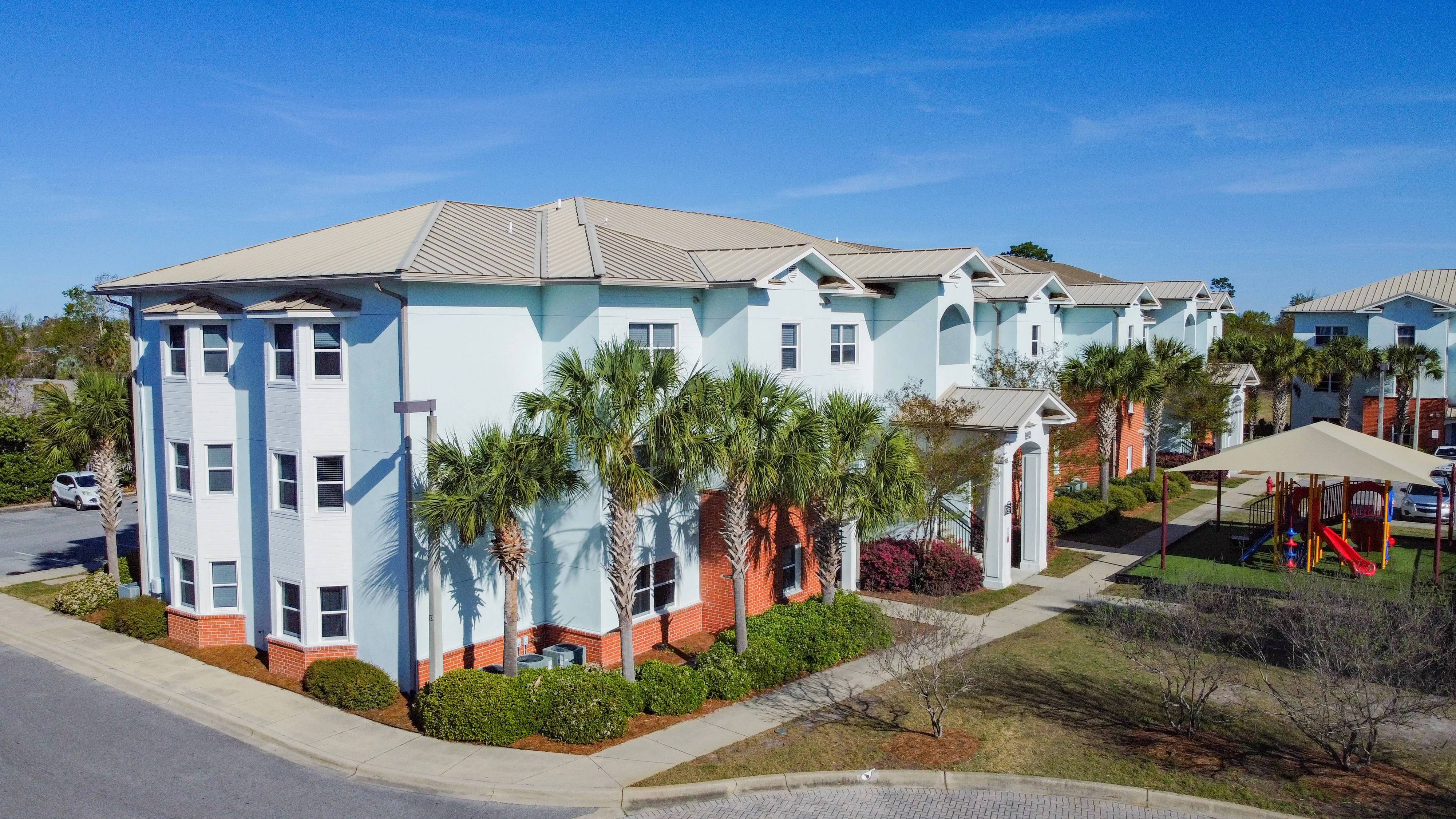 Modern Apartment Complex with Playground Aerial view of a modern apartment complex with palm trees and a playground.