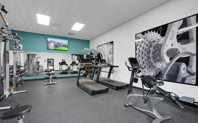 Interior view of a modern gym featuring various exercise equipment, including treadmills and stationary bikes, with a television on the wall.