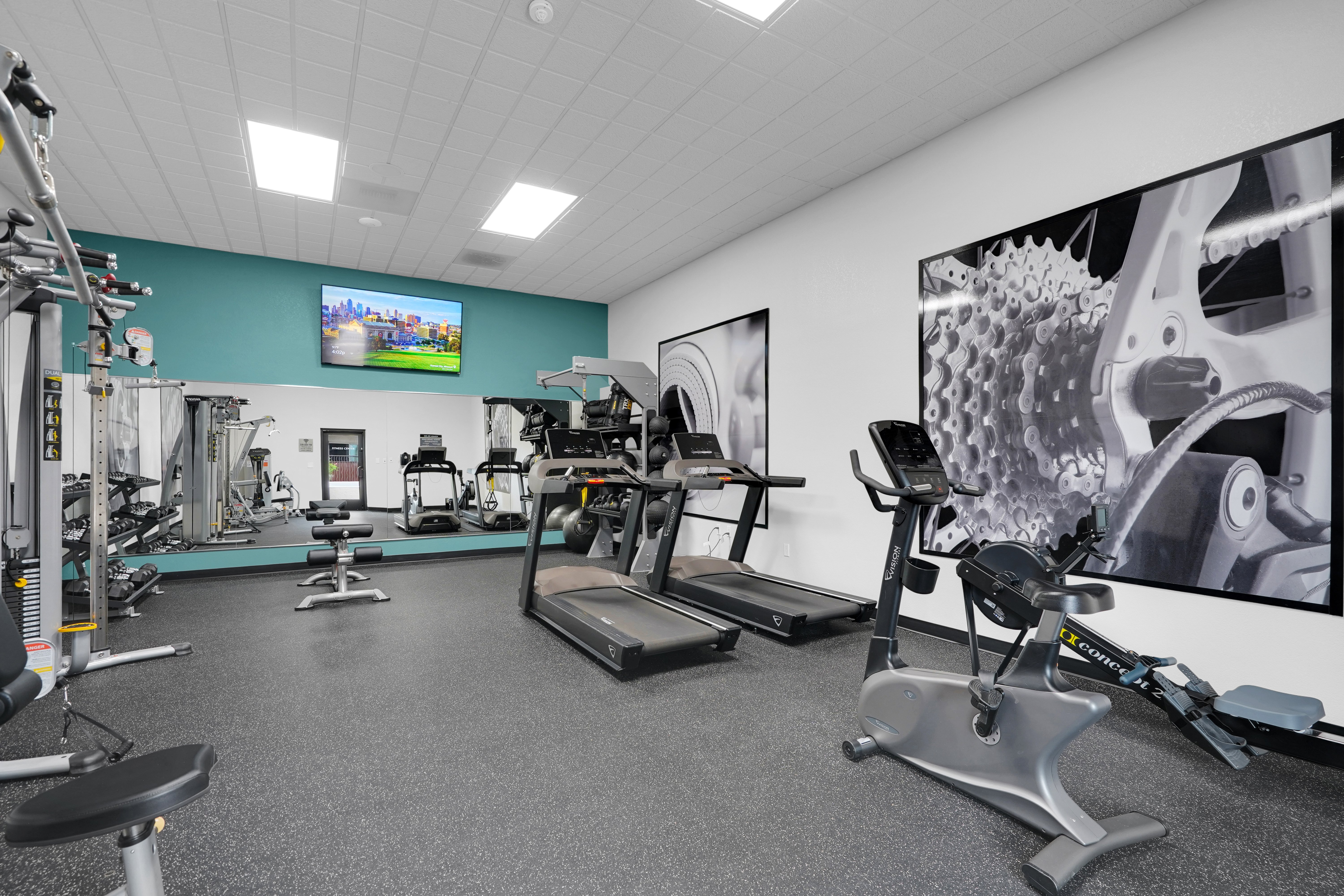 Interior view of a modern gym featuring various exercise equipment, including treadmills and stationary bikes, with a television on the wall.