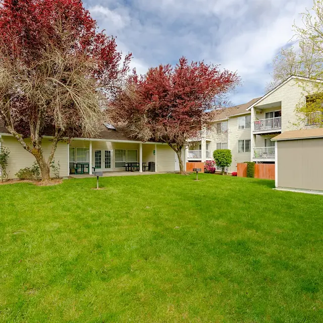 View of a landscaped apartment complex with green lawn and flowering trees.