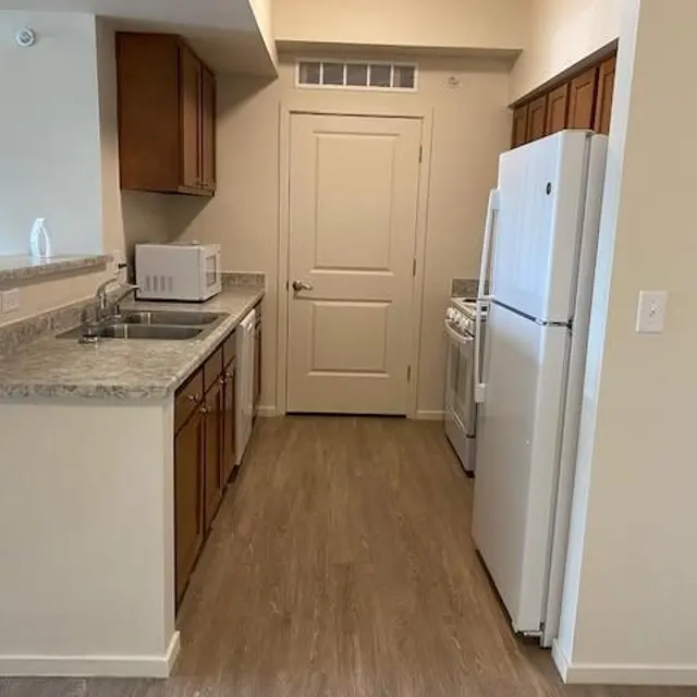 A modern kitchen with wooden cabinets, a white refrigerator, and a countertop made of gray granite.