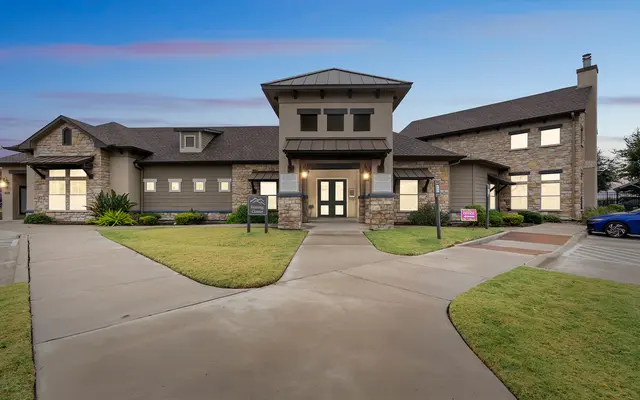 Modern House Front View A modern two-story house with a mix of stone and siding exteriors. It features a prominent front entrance with large windows, a well-maintained lawn, and a paved driveway leading to the entrance.