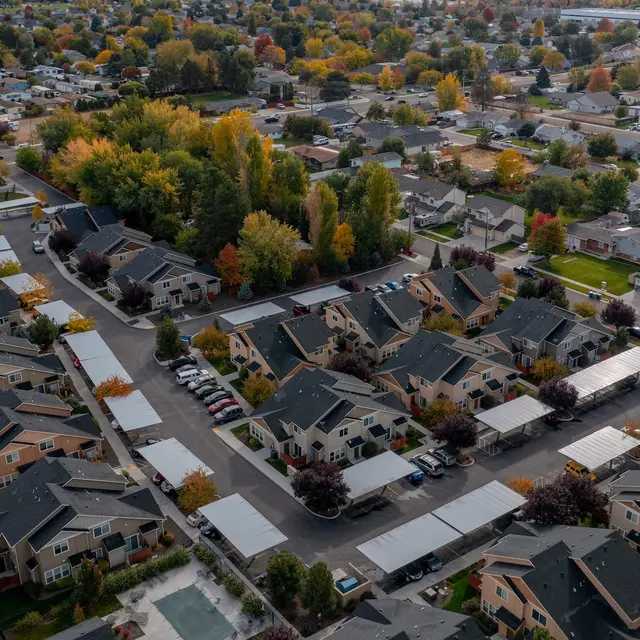 Bowery Point Aerial view of a suburban neighborhood with multiple housing units, trees displaying autumn colors, and a variety of parked cars.