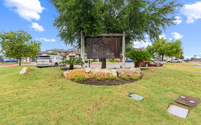 Shiloh Neighborhood Sign A wooden sign reading 'Shiloh' stands in a circular green area, surrounded by rocks and grass. Trees are visible in the background, along with parked vehicles.