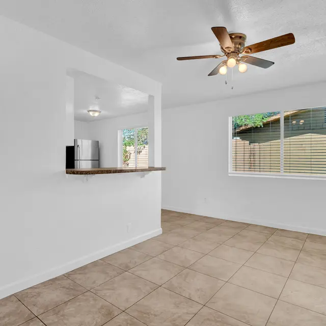 A bright and open living space with tiled floor, ceiling fan, and large window showing outdoor view.