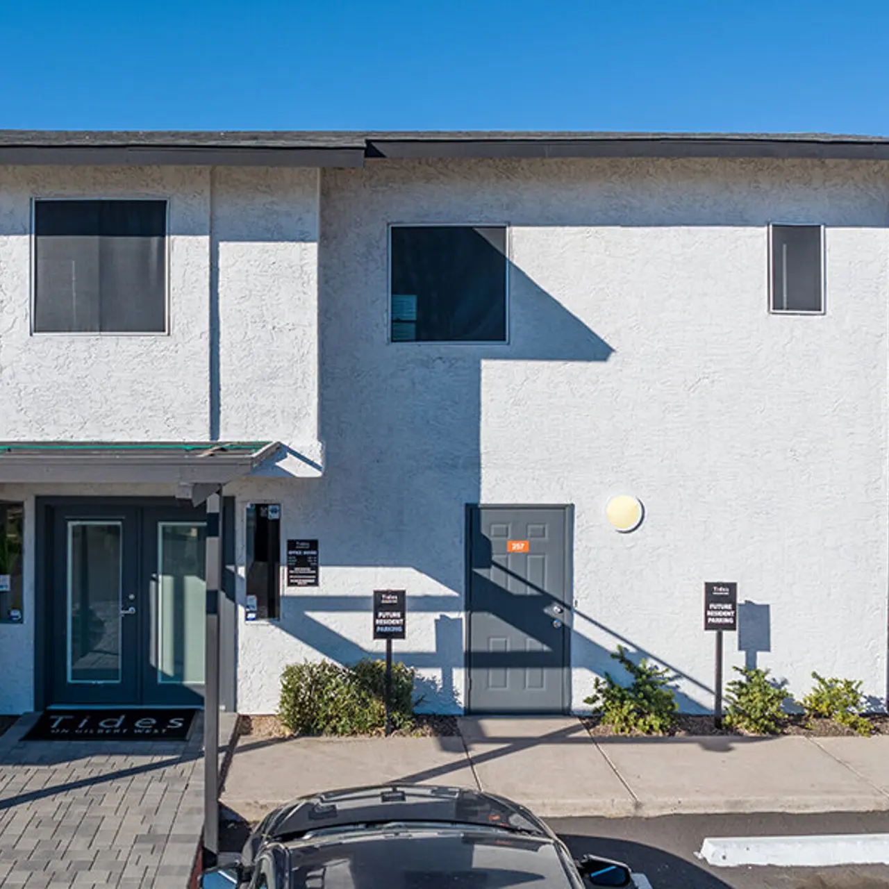 Exterior view of a two-story gray building under clear blue sky, with a small entryway and signage in front.