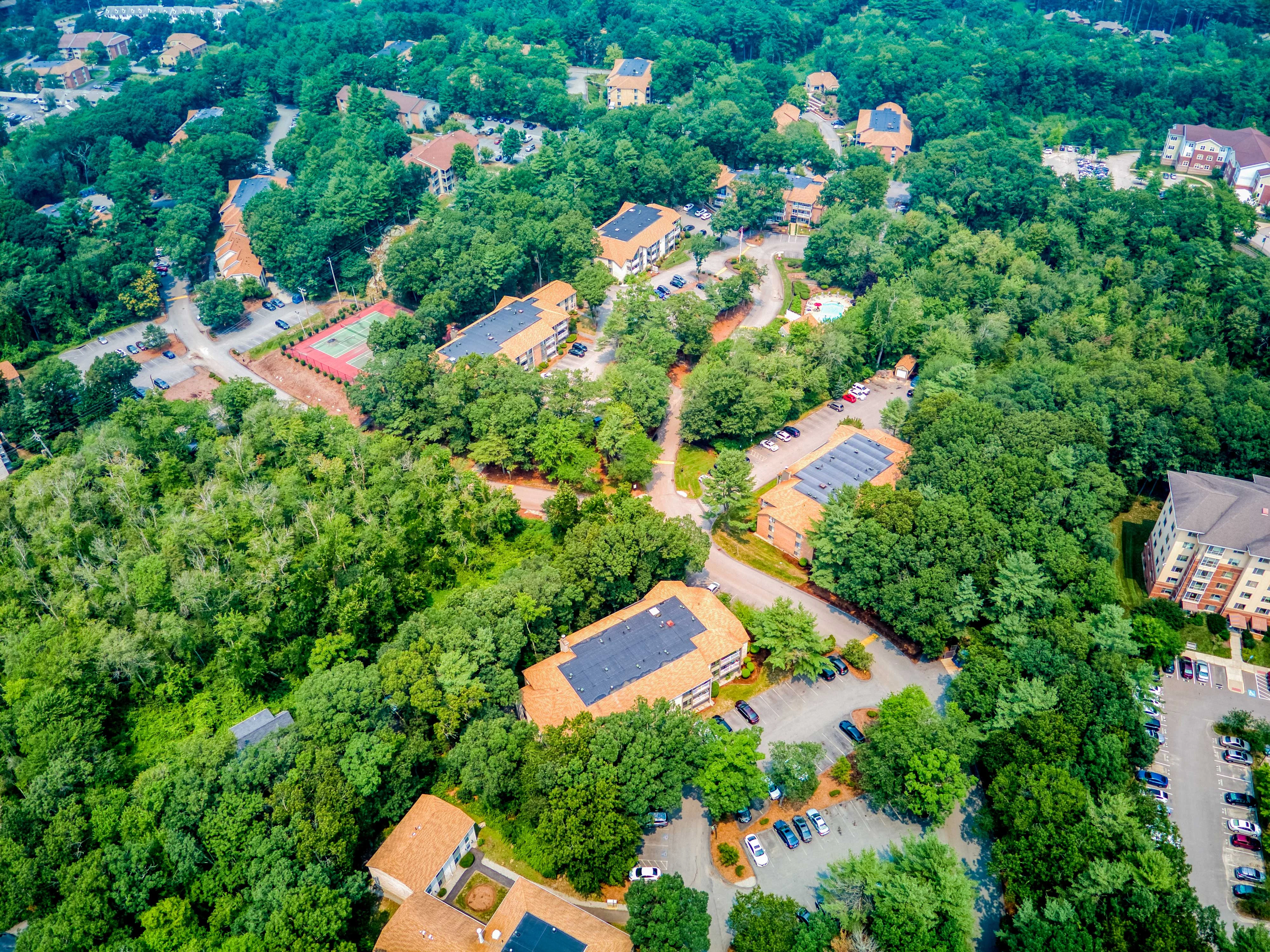 Aerial View of Lush Green Area Aerial view of a green area featuring buildings and parking lots surrounded by trees.