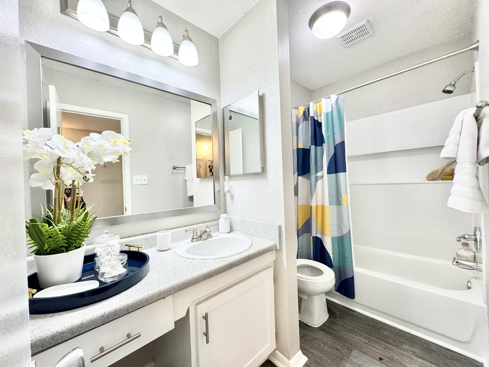 A modern bathroom featuring a bathtub with a colorful shower curtain, a white vanity sink, and decorative plants.