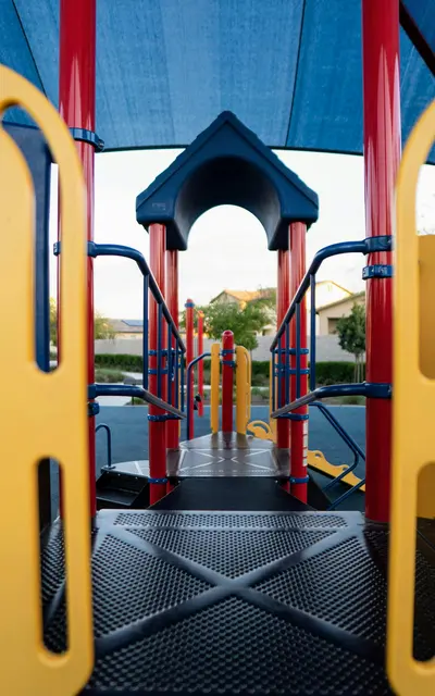 Bayshore Pines View through a playground structure showing colorful play equipment and a shaded area.
