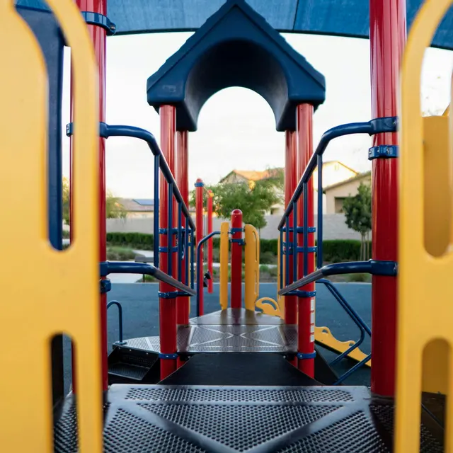 View through a playground structure showing colorful play equipment and a shaded area.