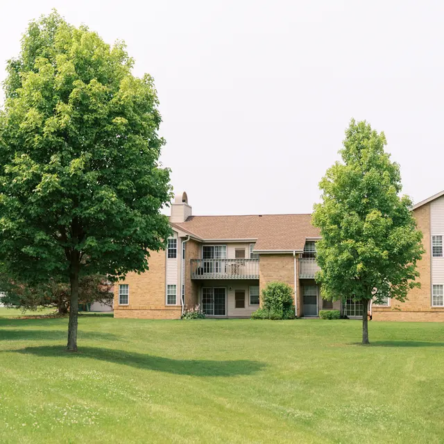 A serene view of an apartment complex surrounded by green lawns and trees.