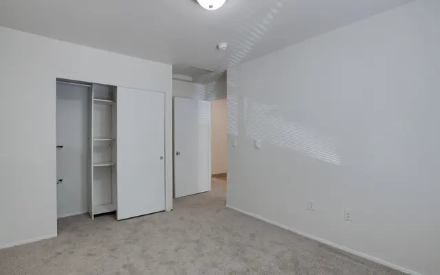 An empty bedroom featuring light-colored walls and carpet.