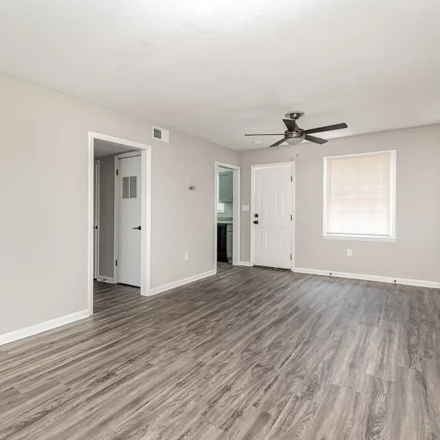 Spacious, empty room with light gray walls, laminate flooring, a ceiling fan, and doors leading to other areas.