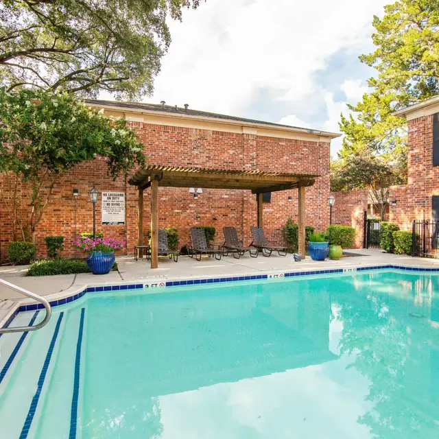 A serene swimming pool area surrounded by brick buildings and green trees.
