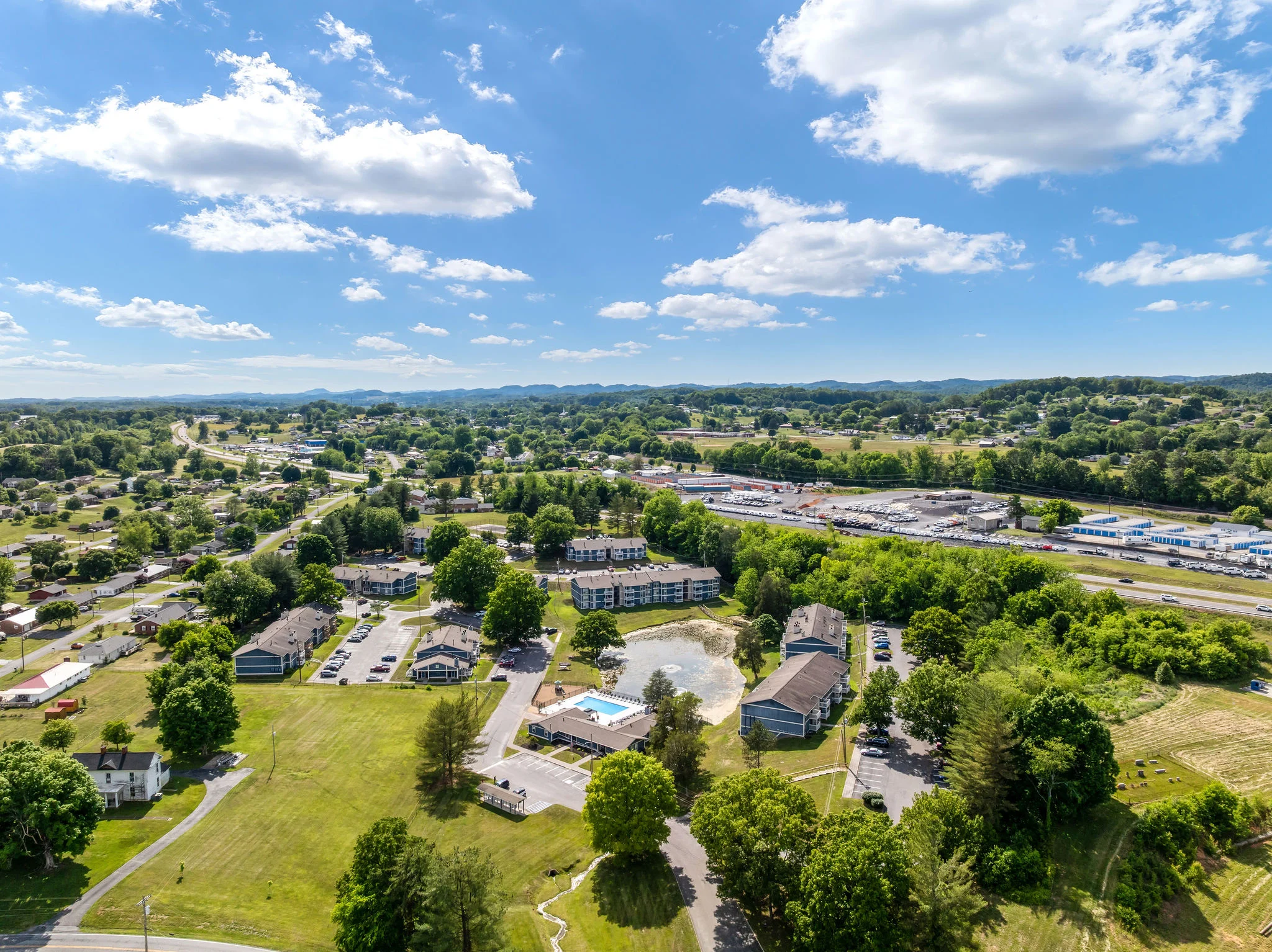 Aerial view of a town showing residential buildings, trees, and open spaces under a clear sky with some clouds.