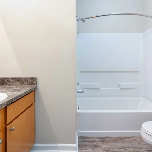 A modern bathroom featuring a wooden vanity with a sink on the left and a white bathtub with shower on the right, both illuminated by natural light.