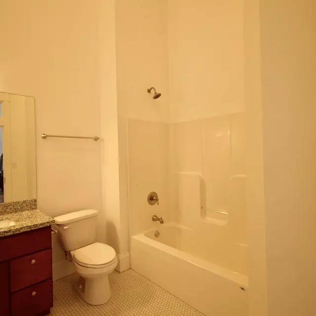 A clean and modern bathroom featuring a shower-tub combination, a toilet, and a sink with a mirrored cabinet. The floor is covered with small, round tiles, and the walls are painted in a light color.