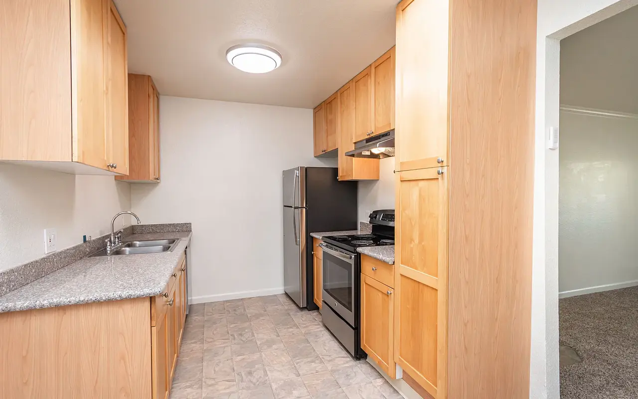 A modern kitchen with wooden cabinets, granite countertop, and stainless steel appliances including a refrigerator, stove, and oven.