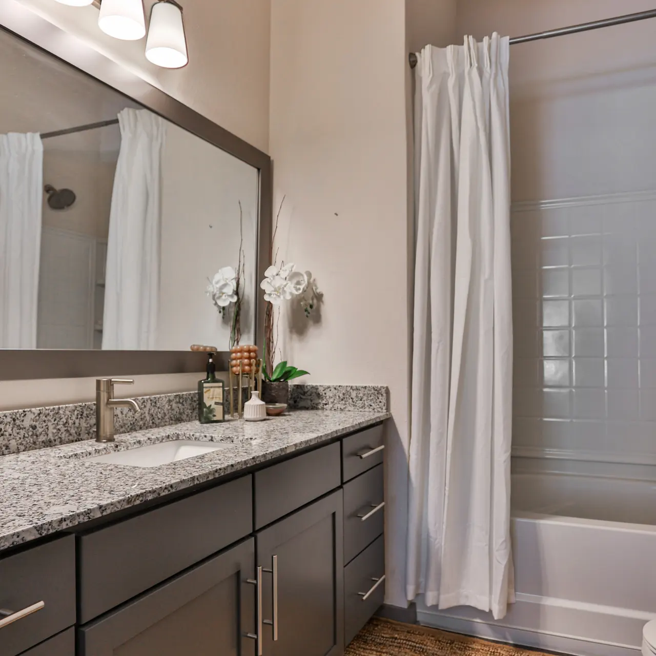 Modern Bathroom Design A modern bathroom featuring a granite countertop with a sink, a large mirror, a bathtub with a shower curtain, and decorative elements including a plant.