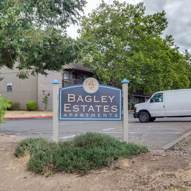 Bagley Estates Apartments Sign Sign for Bagley Estates Apartments with a white van parked nearby and green trees in the background.