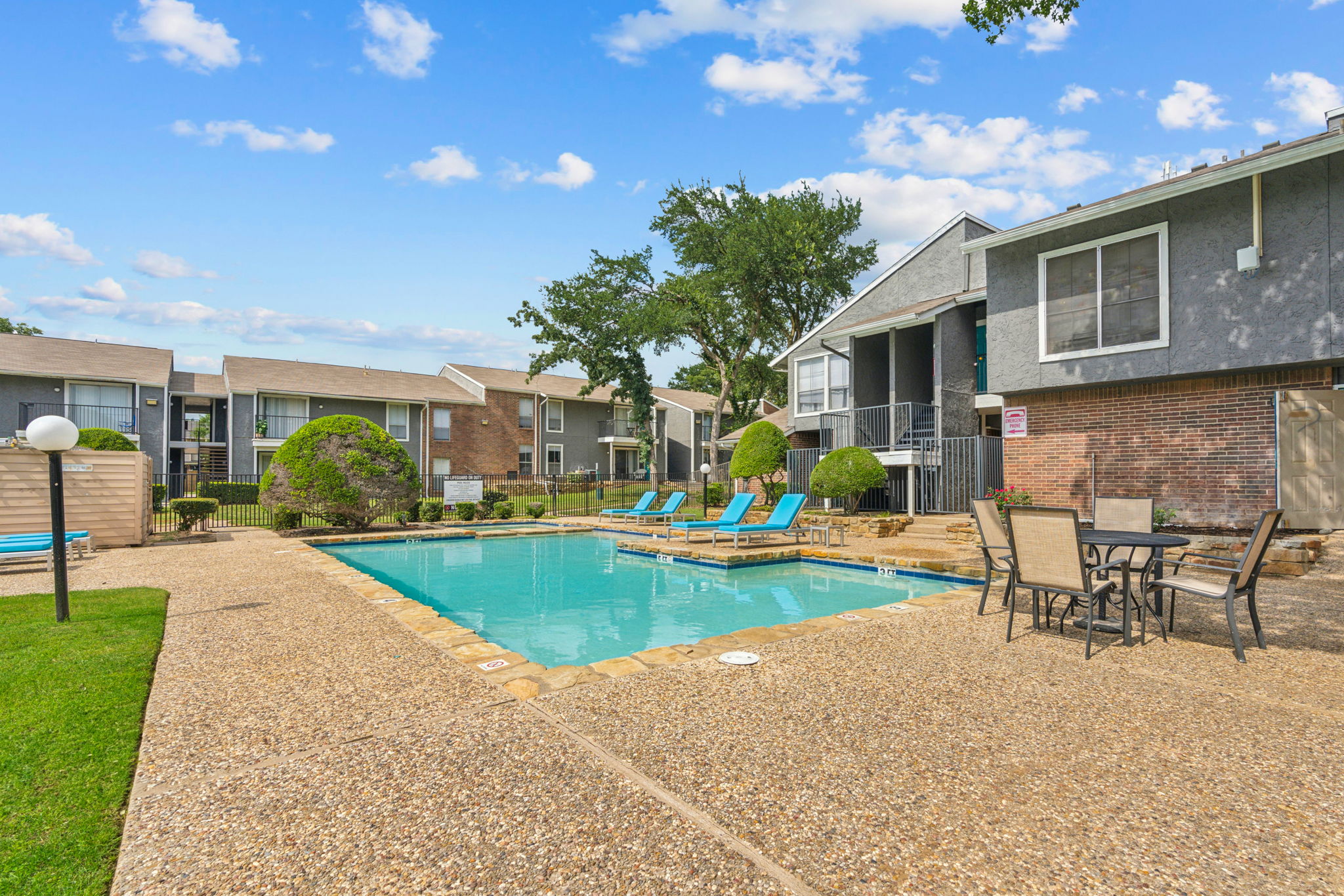 A swimming pool area at an apartment complex surrounded by greenery and residential buildings.