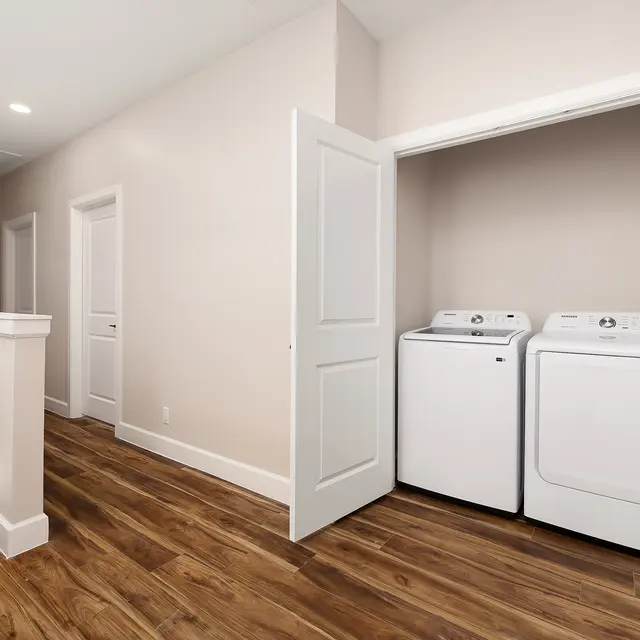 A hallway leading to a laundry area featuring white washing machine and dryer set. The walls are light-colored with a wooden floor.