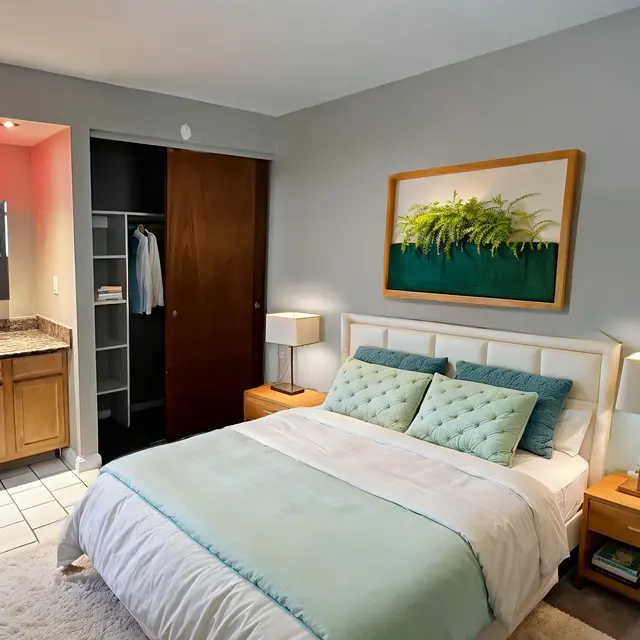 A modern bedroom featuring a bed with soft teal and white linens, nightstands with lamps, a painting on the wall, and an adjoining bathroom area with a sink and a mirror.