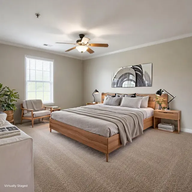 A modern bedroom featuring a wooden bed with gray bedding, a nightstand with lamps, a comfortable chair, and a decorative plant. A ceiling fan hangs above, and a large window allows natural light to fill the space.