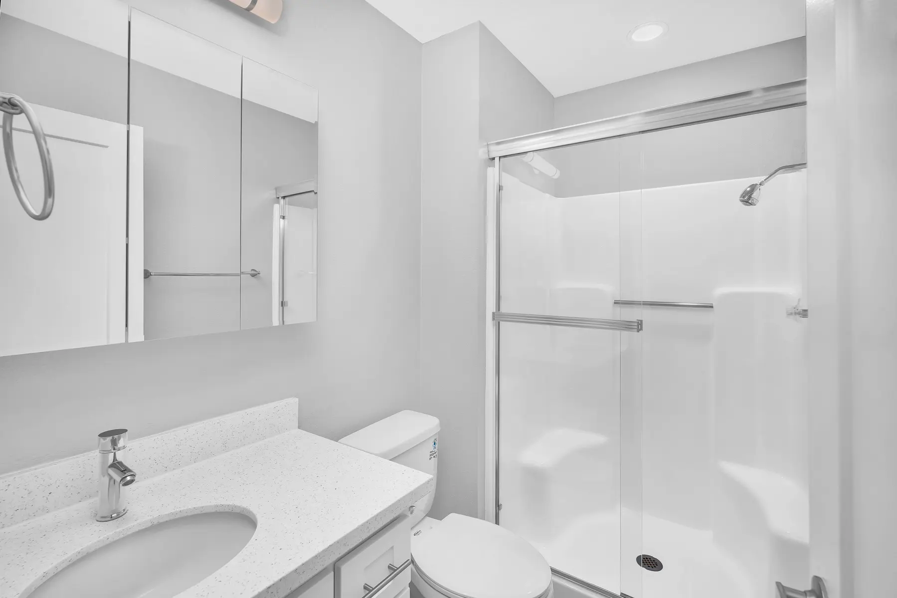 A modern bathroom featuring a white sink, toilet, and a glass shower enclosure. The walls are painted in a light gray color and there are mirrors mounted above the sink. The overall decor is minimalist and clean.