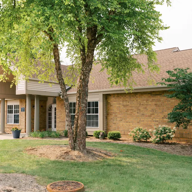 A charming house with a brick exterior and a sloped roof, surrounded by green trees and shrubs.