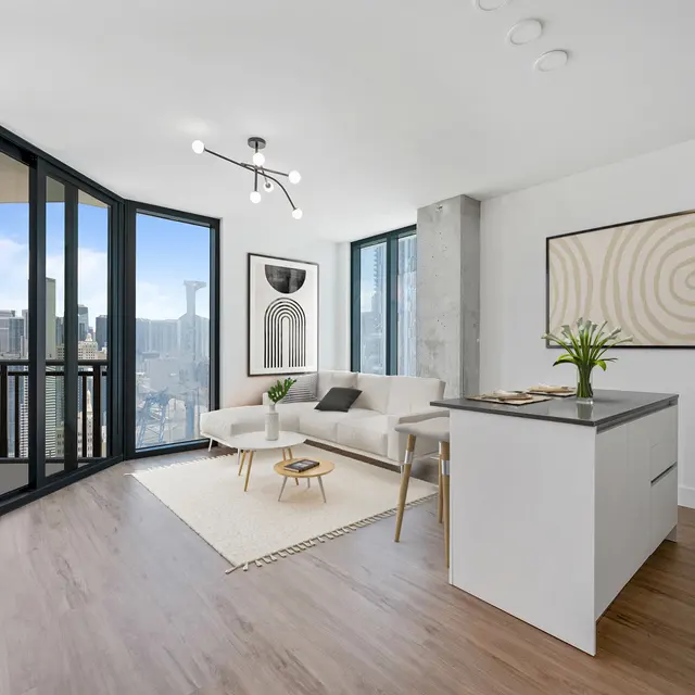 A modern living room with a stylish couch, coffee table, and large windows overlooking a cityscape. There are contemporary artworks on the walls and a small plant on the counter.