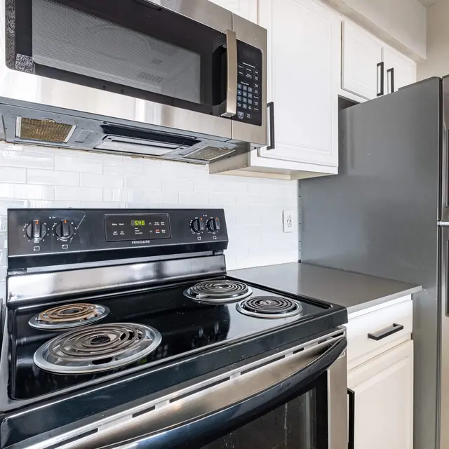 A modern kitchen featuring a stainless steel microwave above a black stove with four burners, next to a silver refrigerator, and white cabinets.