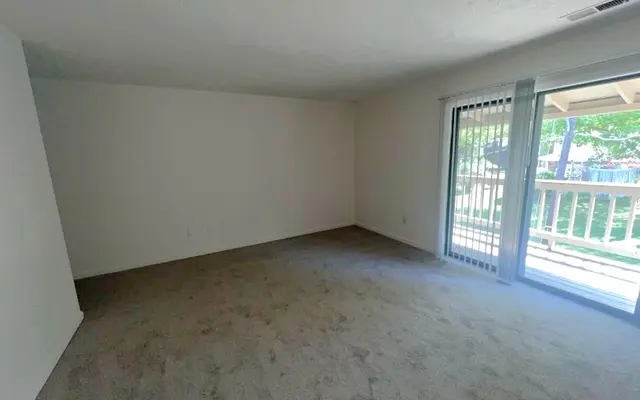Empty Room with Sliding Glass Door A spacious empty room with light beige carpet and white walls, featuring a sliding glass door that leads to a balcony or patio area.