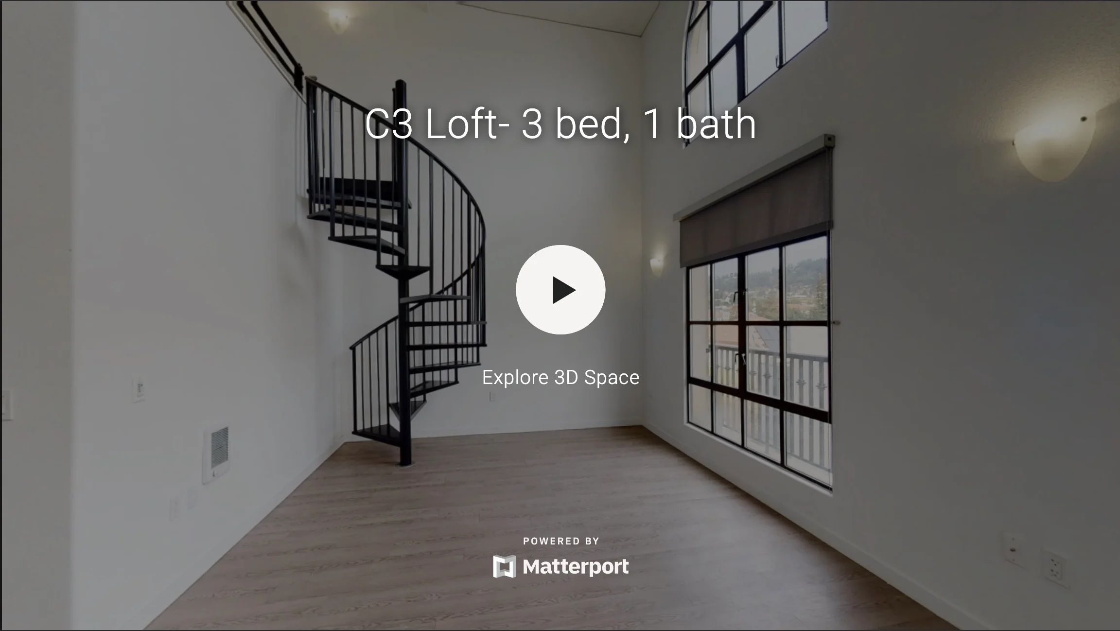 Interior of a modern loft space featuring a spiral staircase and large windows.