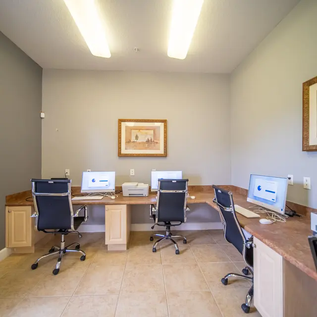 Modern Office Space with Workstations A spacious office area with two desks, each equipped with computers and office chairs. A framed artwork is hanging on the wall, and the floors are tiled.