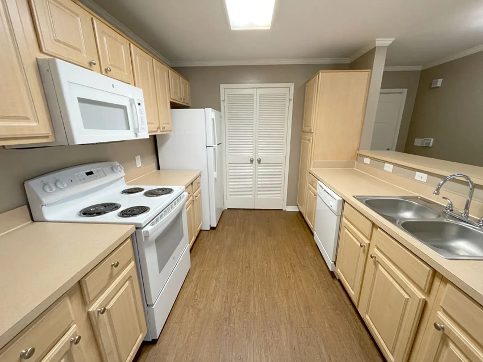 A spacious kitchen featuring light-colored wooden cabinets, a white stove, microwave, and refrigerator, along with a double sink and dishwasher.