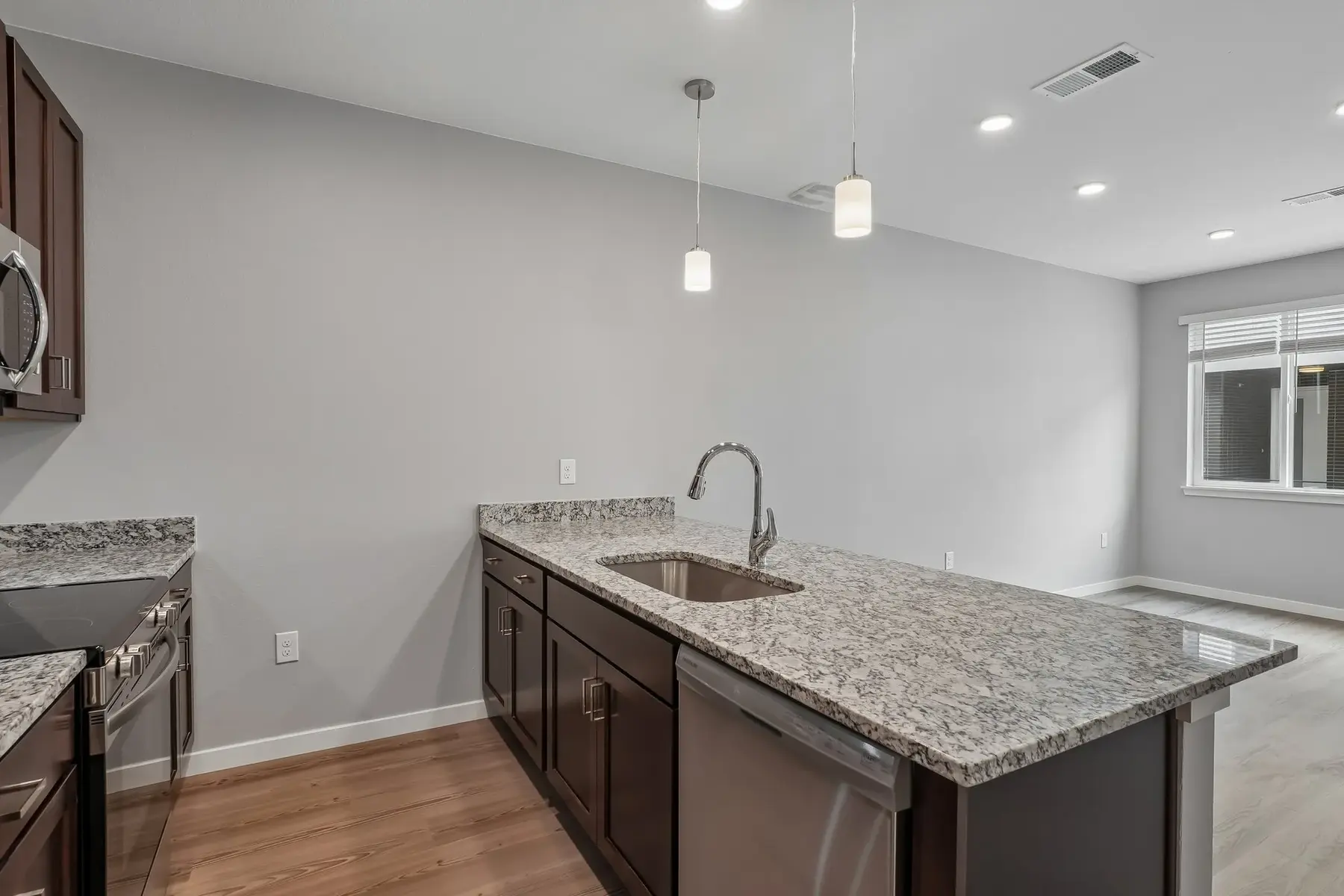 A modern kitchen featuring dark cabinetry and a granite countertop with stainless steel appliances.