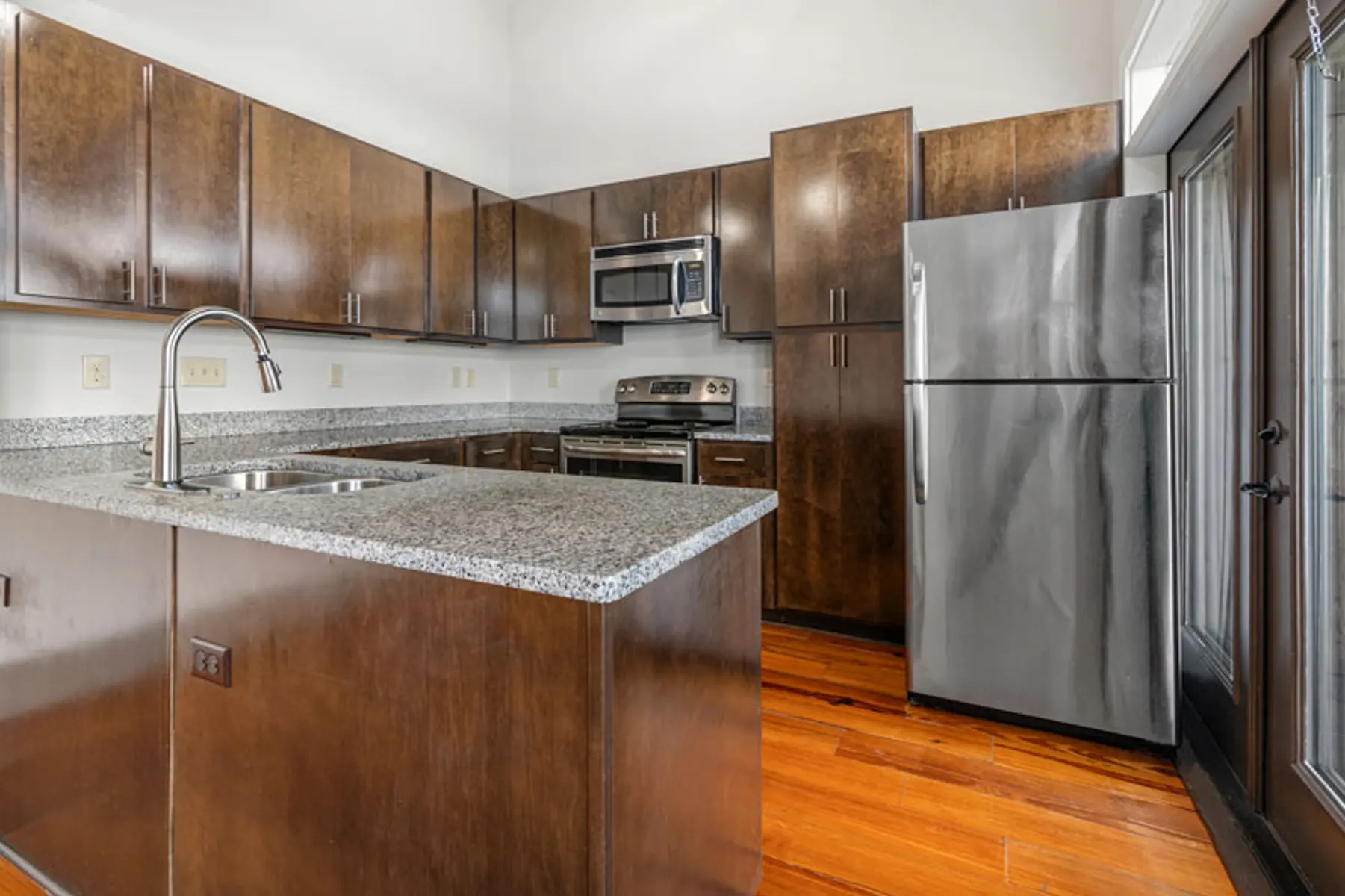 Contemporary kitchen featuring dark wooden cabinetry, stainless steel appliances, and a granite countertop.