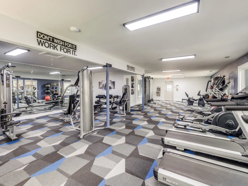 Interior view of a gym featuring various exercise machines, equipment, and motivational wall art.